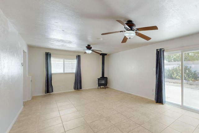 empty room featuring a ceiling fan, light tile patterned floors, and a wood stove