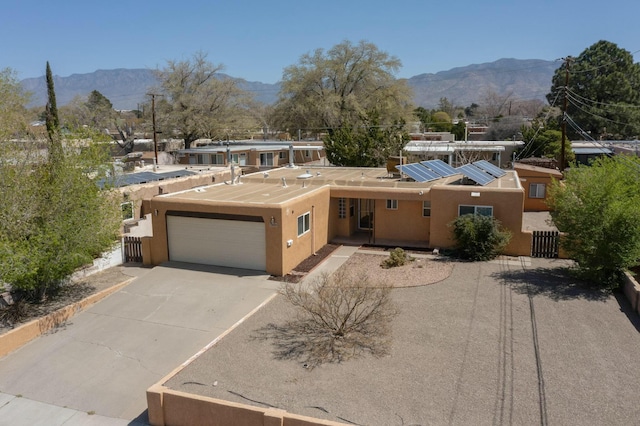 view of front of house with driveway, roof mounted solar panels, a mountain view, an attached garage, and stucco siding