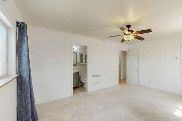 unfurnished bedroom featuring ceiling fan, light colored carpet, and ensuite bath