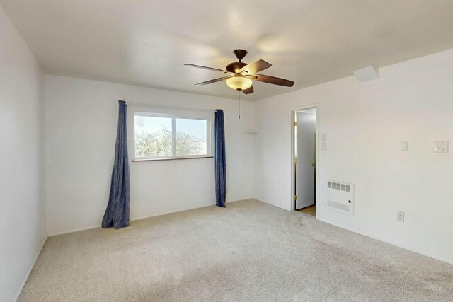 empty room with ceiling fan, heating unit, and light carpet