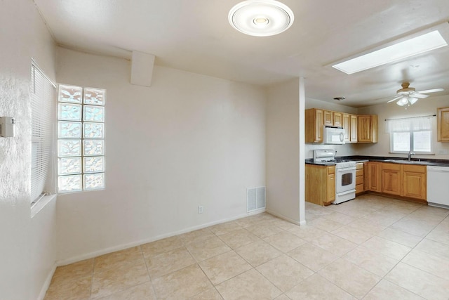kitchen with dark countertops, a sink, white appliances, a skylight, and visible vents