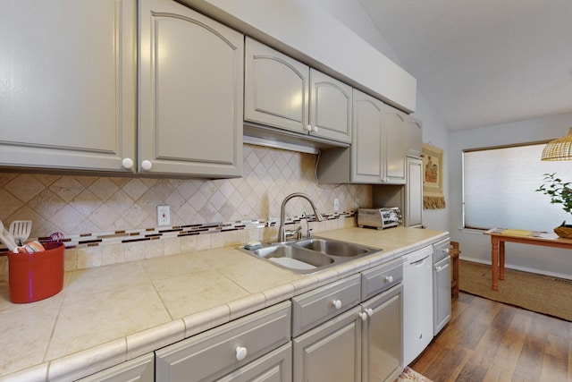 kitchen with tasteful backsplash, dark wood-style flooring, vaulted ceiling, dishwasher, and a sink