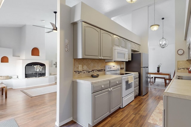 kitchen with gray cabinets, wood finished floors, high vaulted ceiling, and white appliances