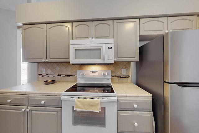 kitchen with tile countertops, backsplash, gray cabinets, and white appliances