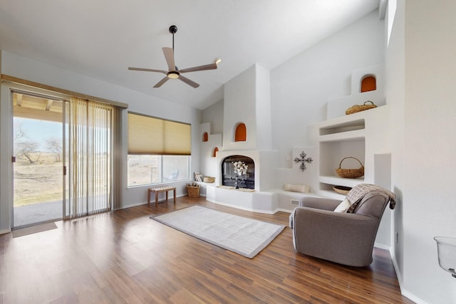 living area featuring baseboards, a ceiling fan, wood finished floors, high vaulted ceiling, and a tile fireplace