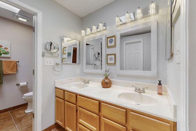 bathroom featuring double vanity, baseboards, a sink, and toilet