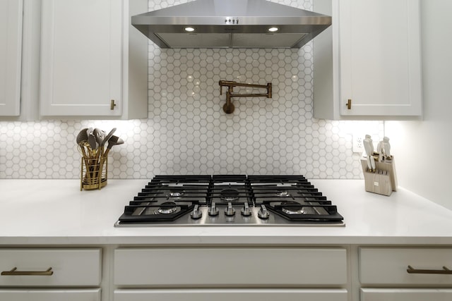 kitchen with stainless steel gas stovetop, range hood, light countertops, and backsplash