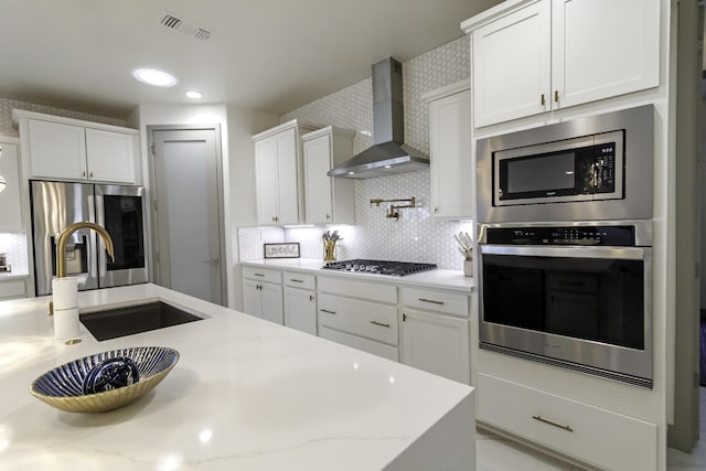 kitchen with wall chimney exhaust hood, white cabinetry, visible vents, appliances with stainless steel finishes, and a sink