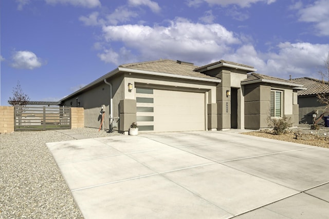 prairie-style home featuring a garage, fence, stucco siding, a gate, and driveway