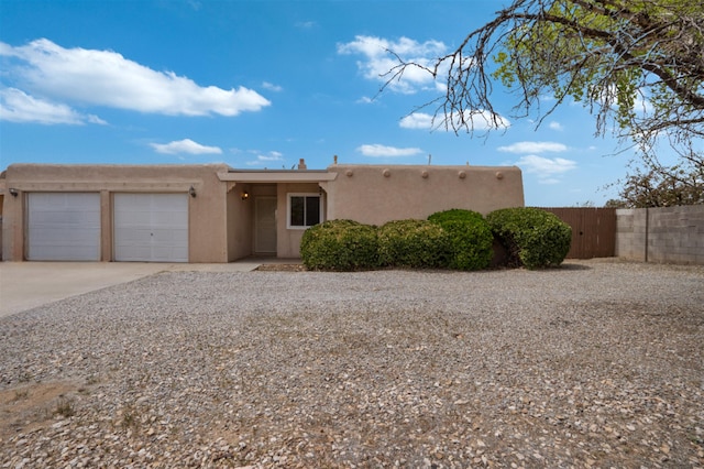 adobe home featuring an attached garage, driveway, fence, and stucco siding