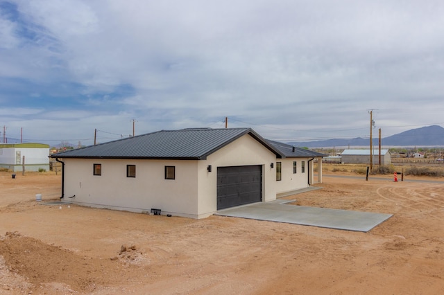 view of property exterior featuring a mountain view, driveway, metal roof, an attached garage, and stucco siding