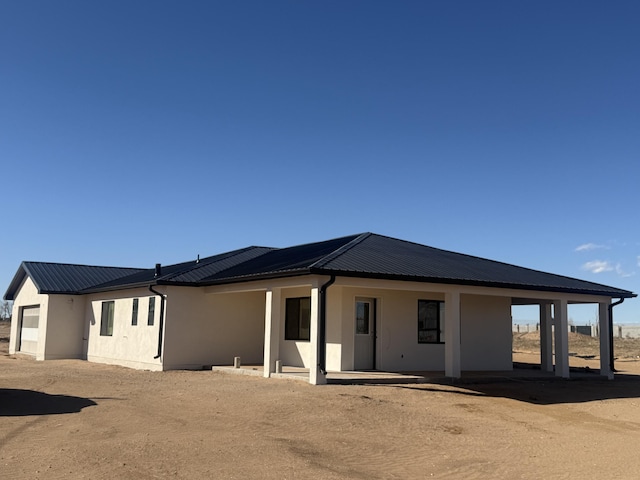back of house with stucco siding and metal roof