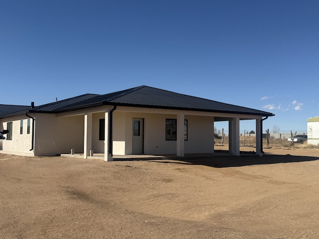 back of house with stucco siding and metal roof