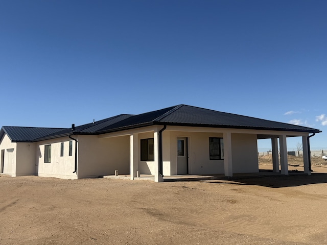 back of house featuring stucco siding and metal roof