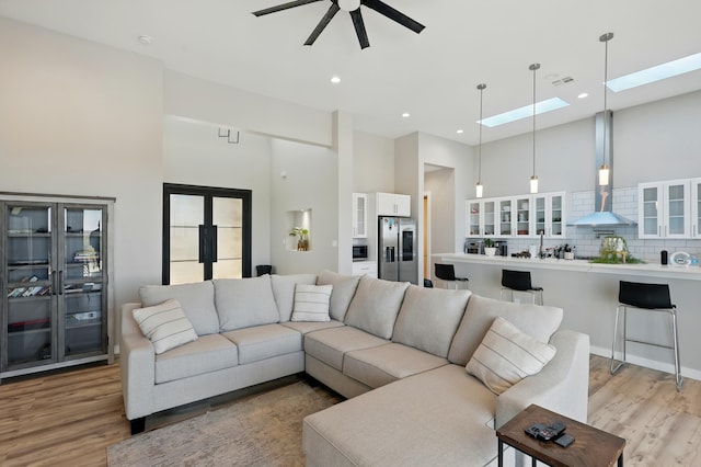 living area featuring visible vents, a towering ceiling, a ceiling fan, light wood-style flooring, and a skylight