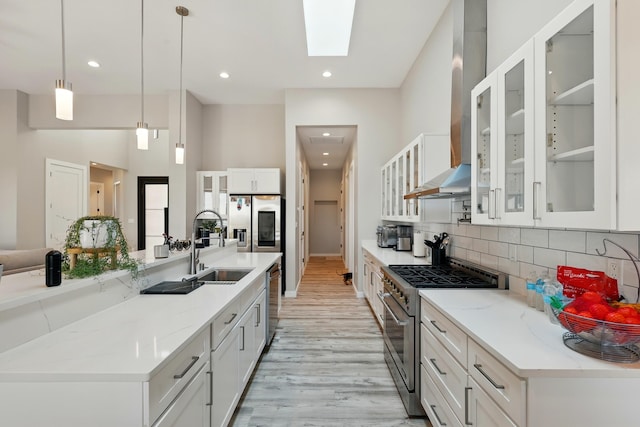 kitchen featuring a skylight, appliances with stainless steel finishes, a sink, light wood finished floors, and wall chimney exhaust hood