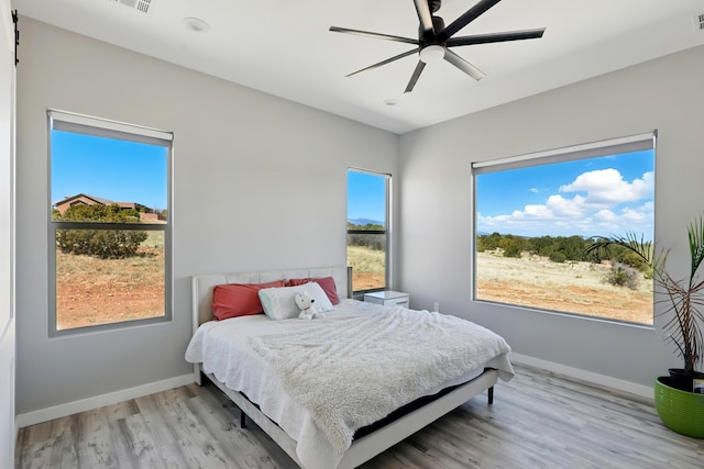 bedroom featuring baseboards, multiple windows, a ceiling fan, and light wood-type flooring