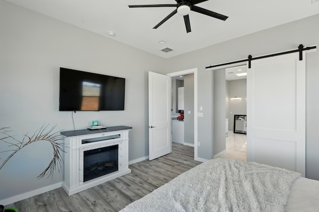 bedroom with light wood-type flooring, a barn door, and visible vents