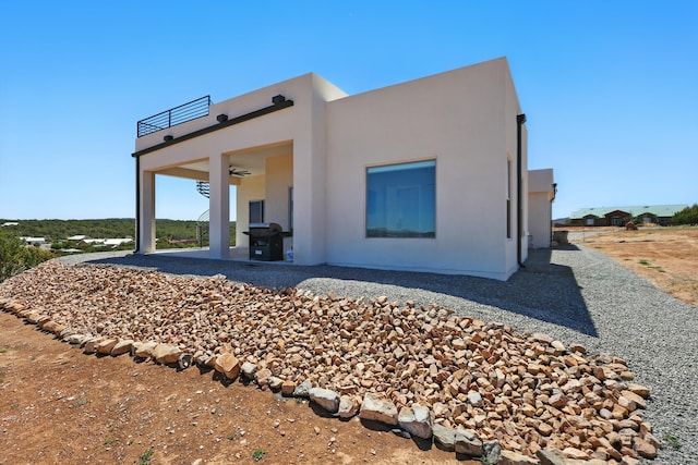 rear view of property with a ceiling fan, a patio area, stucco siding, and a balcony