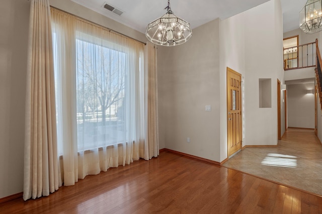unfurnished dining area with light wood-type flooring, a notable chandelier, baseboards, and visible vents