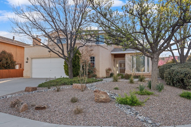 view of front of house featuring an attached garage, driveway, stucco siding, and fence