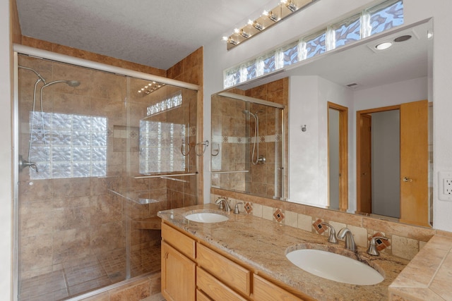 full bath with double vanity, visible vents, a shower stall, and a sink