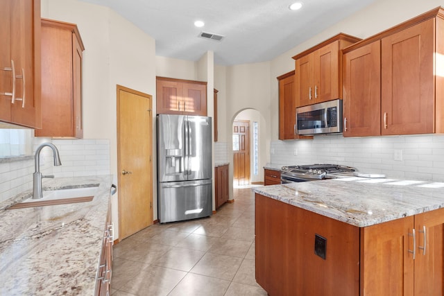 kitchen featuring brown cabinetry, stainless steel appliances, light stone counters, and a sink