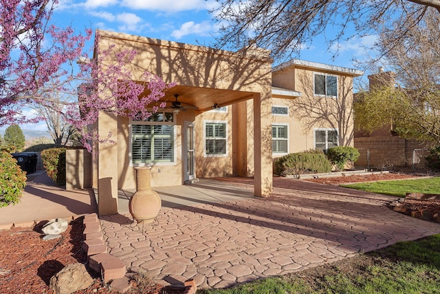 view of front of house featuring fence, a patio area, a ceiling fan, and stucco siding