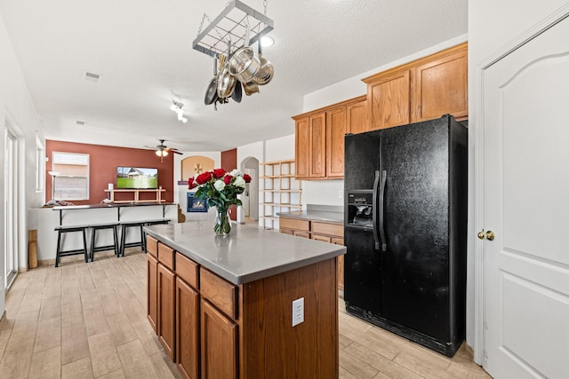 10532 Box Canyon Pl NW, Albuquerque, NM 87114 - kitchen featuring black fridge with ice dispenser, a kitchen island, light wood-style flooring, ceiling fan, and brown cabinets