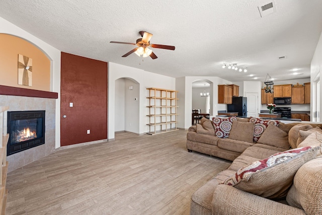 10532 Box Canyon Pl NW, Albuquerque, NM 87114 - living area with ceiling fan, light wood-style flooring, arched walkways, a textured ceiling, and a tiled fireplace