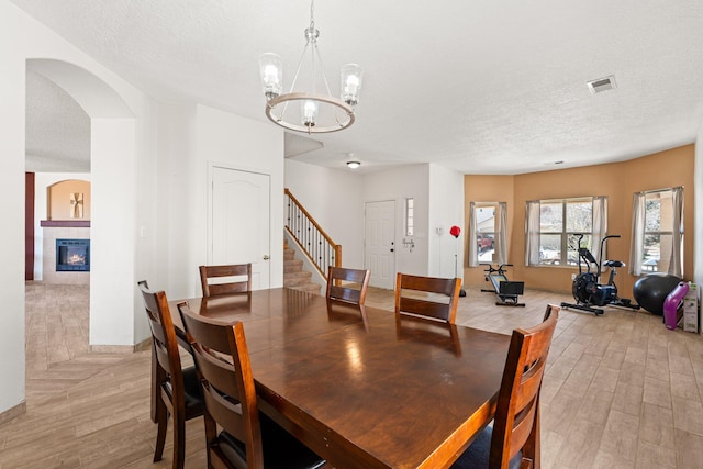 10532 Box Canyon Pl NW, Albuquerque, NM 87114 - dining room with light wood finished floors, a chandelier, a textured ceiling, stairs, and a tile fireplace