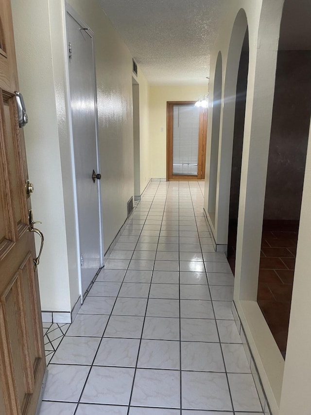 corridor with a textured ceiling, visible vents, and light tile patterned floors