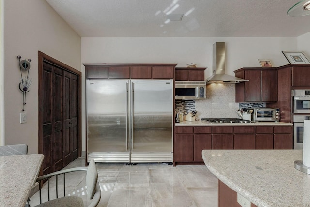 kitchen featuring a toaster, light countertops, appliances with stainless steel finishes, and wall chimney exhaust hood