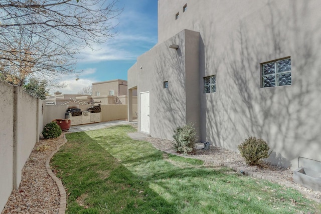 view of side of home with a patio, a fenced backyard, stucco siding, and a lawn