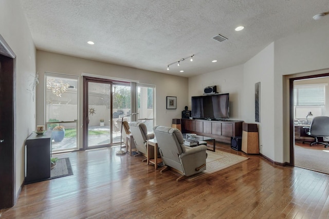 living room featuring a textured ceiling, wood finished floors, visible vents, and recessed lighting