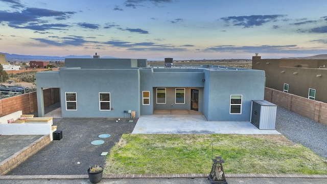 4621 27th Ave NE, Rio Rancho, NM 87144 - back of house at dusk with a fenced backyard, a patio area, stucco siding, and a shed