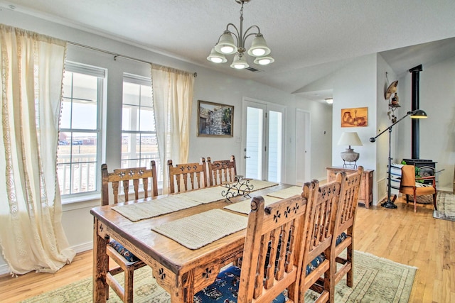 dining room featuring a textured ceiling, light wood-type flooring, a chandelier, lofted ceiling, and a wood stove