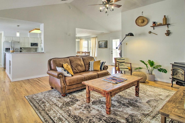 living area with light wood finished floors, baseboards, a ceiling fan, high vaulted ceiling, and a wood stove