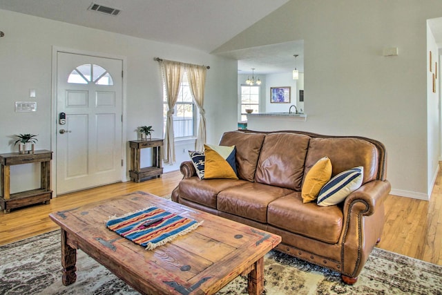 living area featuring a chandelier, light wood finished floors, baseboards, lofted ceiling, and visible vents