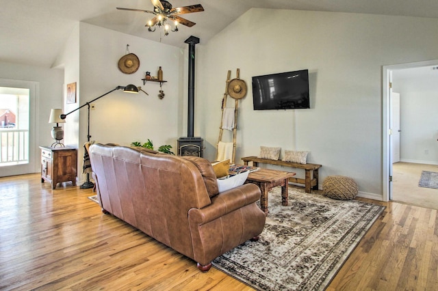 living area with light wood-type flooring, vaulted ceiling, baseboards, ceiling fan, and a wood stove