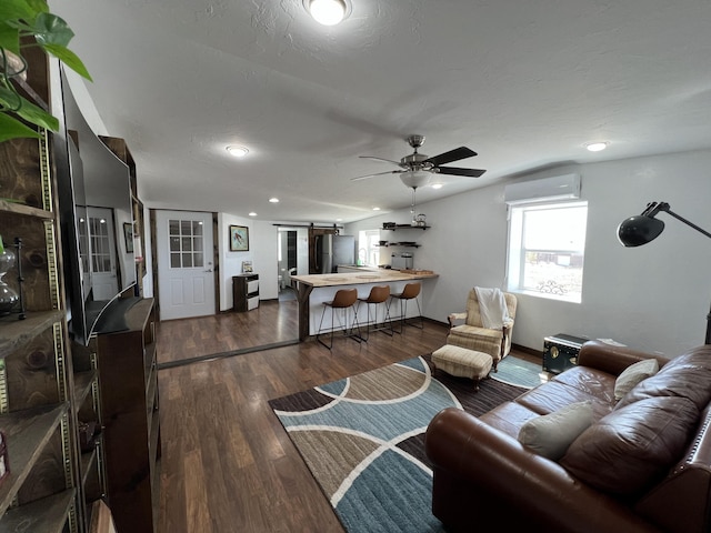 living room featuring a barn door, dark wood-style flooring, a ceiling fan, and a wall unit AC