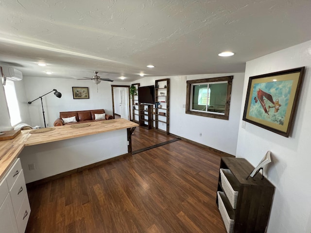 living area with recessed lighting, a ceiling fan, a wall unit AC, dark wood-type flooring, and baseboards