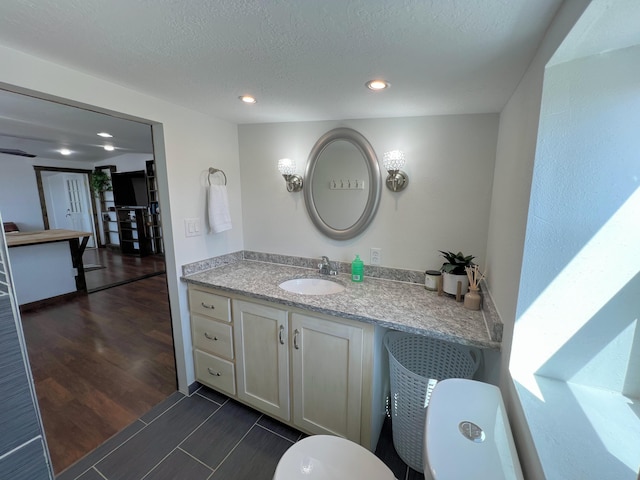 bathroom with recessed lighting, wood finished floors, toilet, vanity, and a textured ceiling