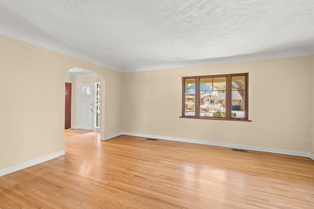 spare room with light wood finished floors, visible vents, arched walkways, baseboards, and a textured ceiling