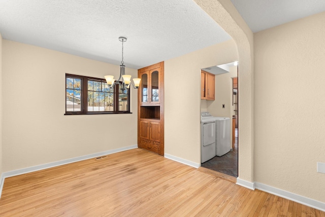 unfurnished dining area featuring light wood finished floors, arched walkways, visible vents, a chandelier, and separate washer and dryer