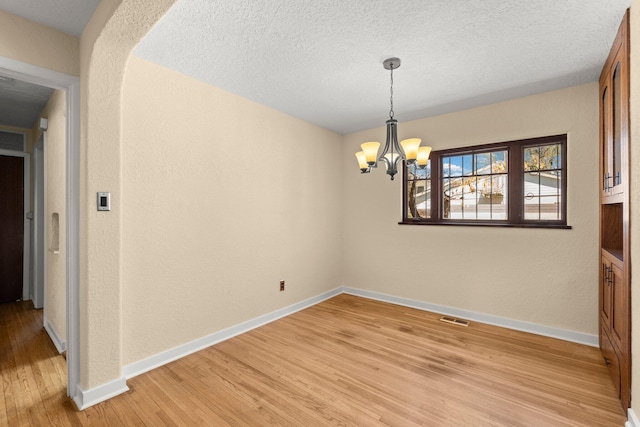empty room featuring a textured ceiling, visible vents, baseboards, a chandelier, and light wood-style floors
