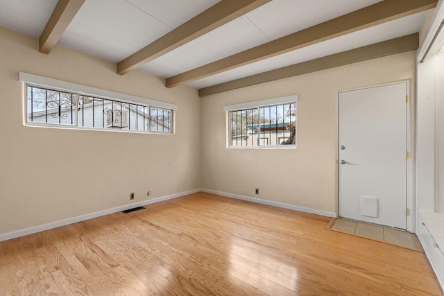 unfurnished room with beamed ceiling, wood finished floors, visible vents, and a healthy amount of sunlight