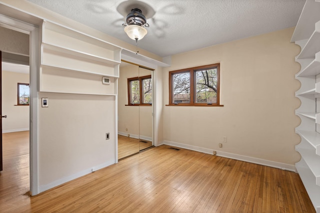 empty room with visible vents, light wood-style floors, baseboards, a textured ceiling, and ceiling fan