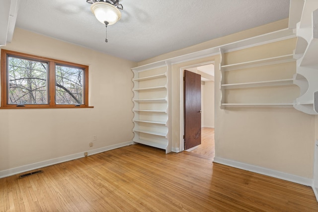 unfurnished bedroom with baseboards, wood finished floors, and visible vents