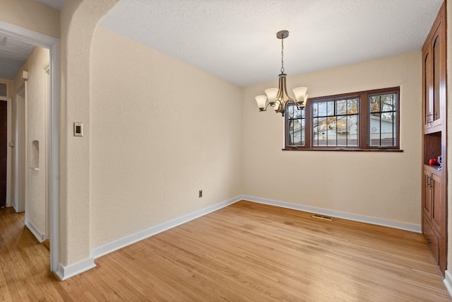 unfurnished dining area with light wood-style floors, a textured wall, baseboards, a notable chandelier, and visible vents